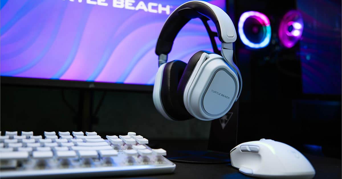 Gaming-opsætning med en computerskærm med lilla grafik, et hvidt tastatur, en hvid gaming-mus og Turtle Beach-headset på et stativ.