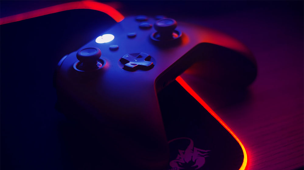 Et nærbillede af en gaming-controller oplyst af blå og røde neonlys, der delvist hviler på en dragedesignet musemåtte, sætter scenen for enhver "Can I Run It"-gamingsession.